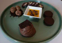 Four preparations of Chocolate. Cocolate pudding with kiwicha (amaranth) and chocolate crisp, chocolate truffles, chocolate "salami", and chocolate alfajores. Maracuya coulis with cocoa nibs in the center